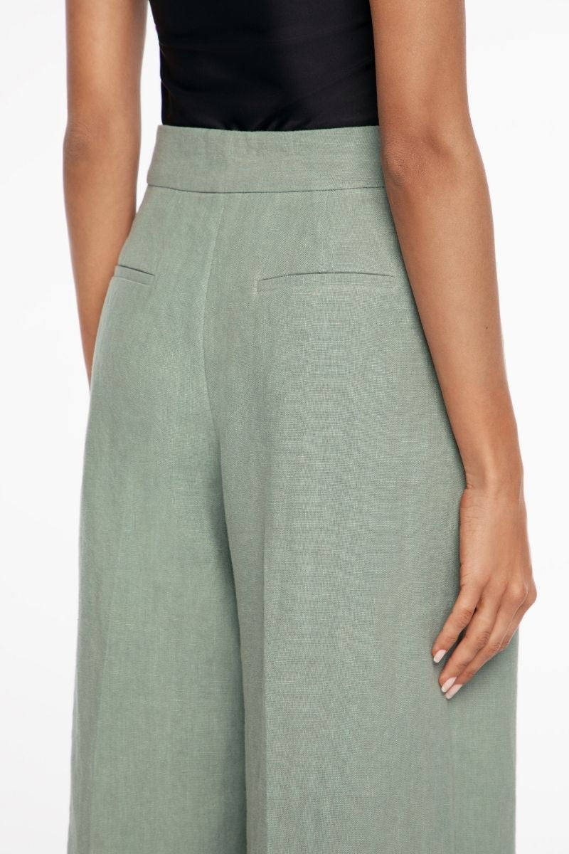 Light beige linen wide-leg pants by Dāl the Label hanging on a wooden hanger, showcasing relaxed fit and breathable fabric.