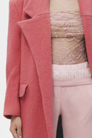 Pink wool maxi coat by JC Pajares hanging on a wooden hanger, showcasing its length and soft fabric texture.