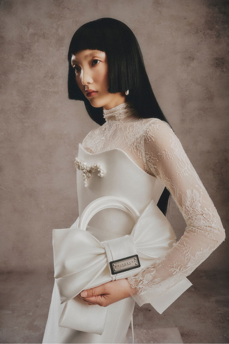 Ivory bow top handle bag by White Plan, stylish and elegant accessory with a bow detail and structured design.