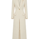 Maison Des Copains ivory cream V-neck trench coat with classic collar and belted waist, displayed hanging on a clothing rack.