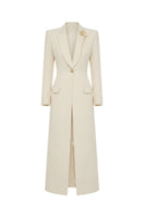 Maison Des Copains ivory cream V-neck trench coat with classic collar and belted waist, displayed hanging on a clothing rack.