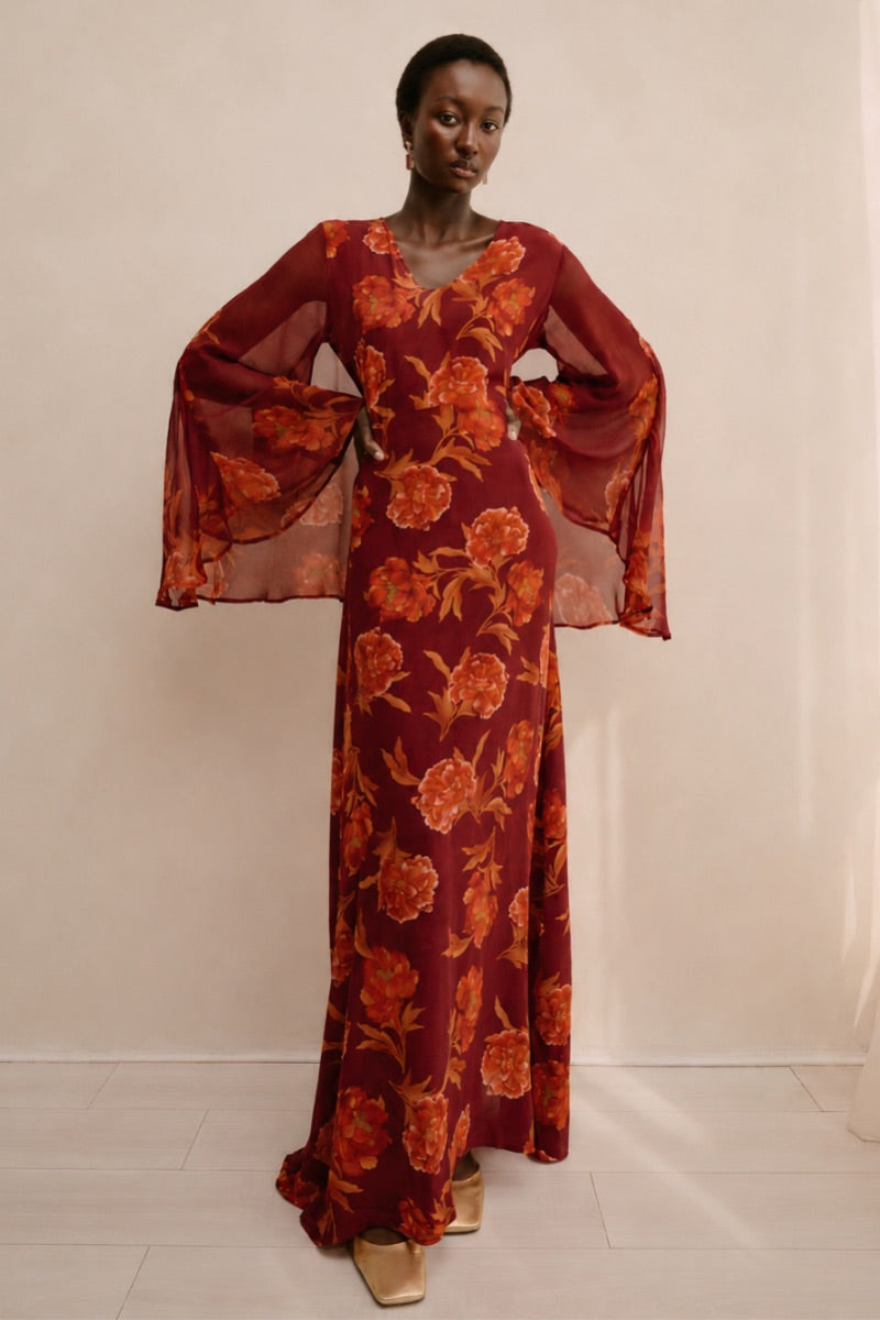 Red Raishma Karina maxi dress hanging on a wooden hanger, showcasing elegant fabric and flowing silhouette.