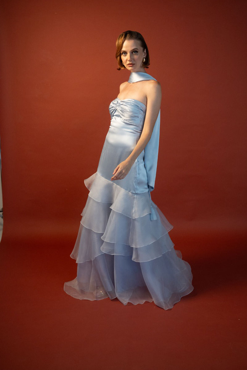 Sky blue Anne gown by Estefania, flowing fabric with elegant design, displayed on a hanger with detailed bodice and full skirt.