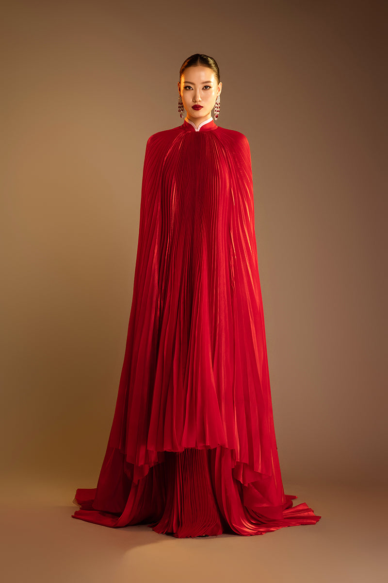 Red Valenciani SUNRAY pleated high-neck cape gown displayed on a hanger, showcasing elegant pleats and flowing fabric.