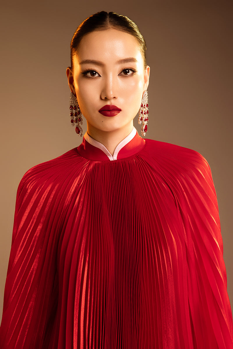 Red Valenciani SUNRAY pleated high-neck cape gown displayed on a model with flowing fabric and elegant design.