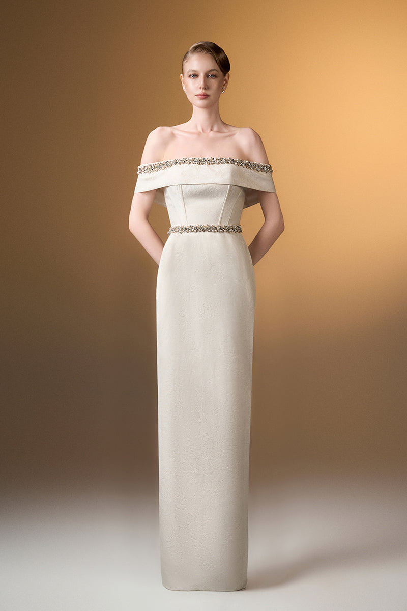 Ivory off-shoulder column gown in rose design brocade by I.H.F, featuring elegant draping and intricate floral pattern.