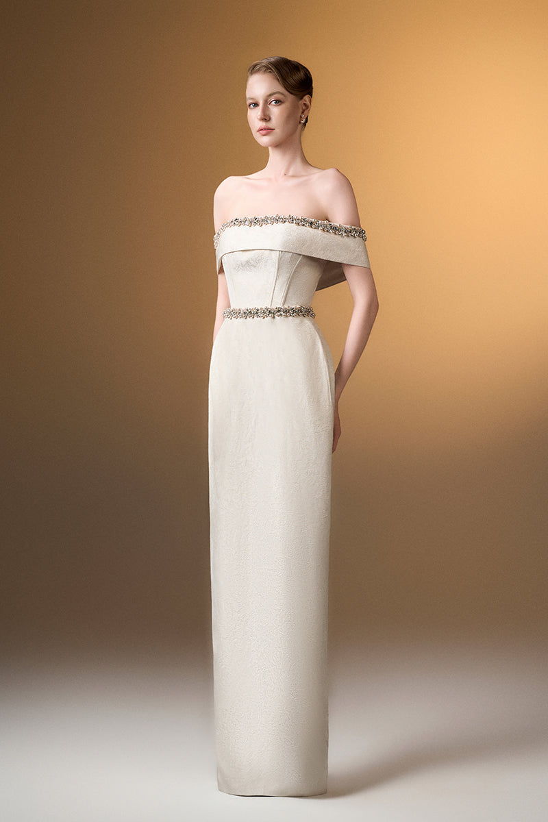 Ivory off-shoulder column gown in rose design brocade by I.H.F, featuring elegant draped fabric and intricate floral pattern.