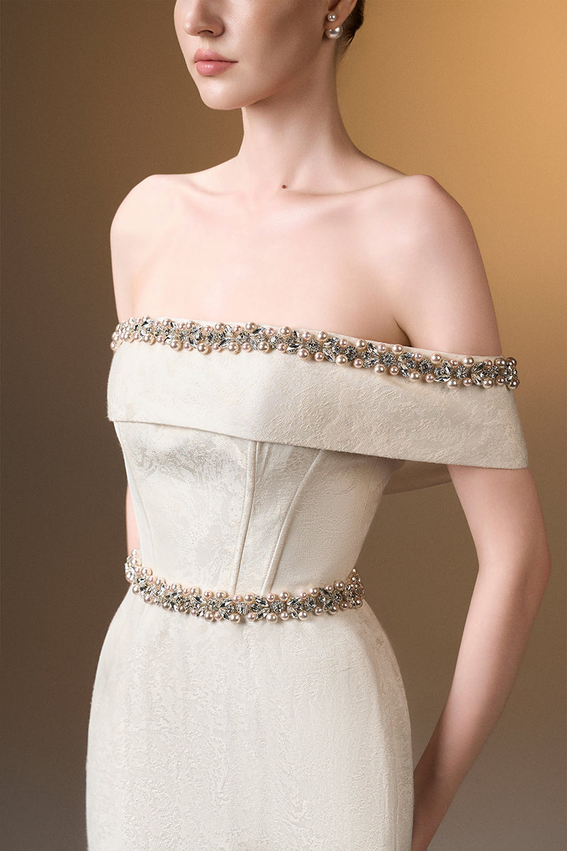 Ivory off-shoulder column gown in rose design brocade by I.H.F, featuring elegant draping and intricate floral detailing.