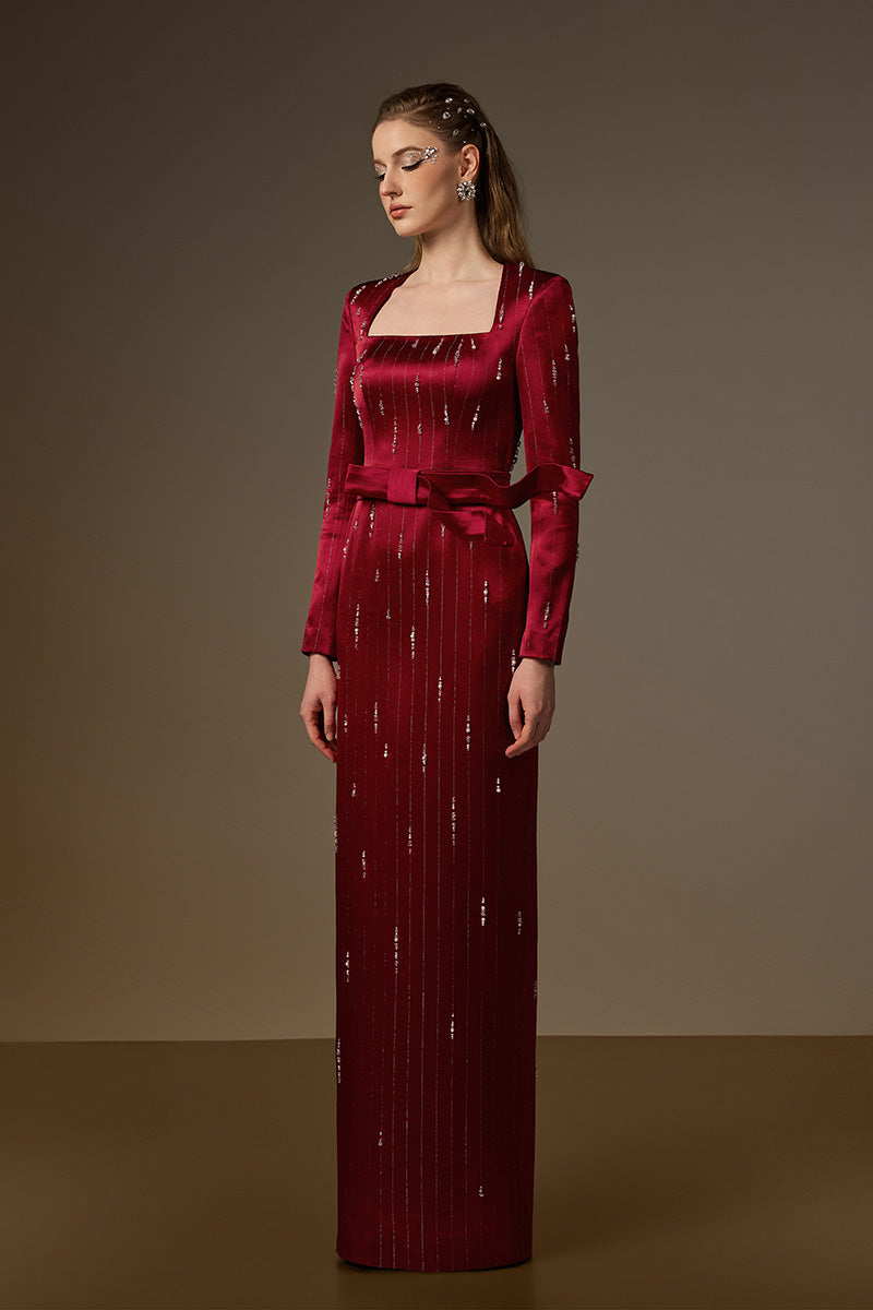 Red metallic belted train column gown by I.H.F featuring a trapeze neckline and flowing, wind-blown style in shimmering silk fabric.