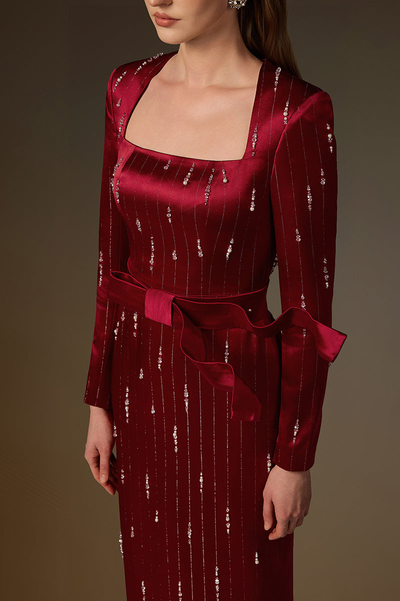Red metallic belted train column gown by I.H.F with a trapeze neck, flowing silhouette, and wind-blown train effect in silk fabric.