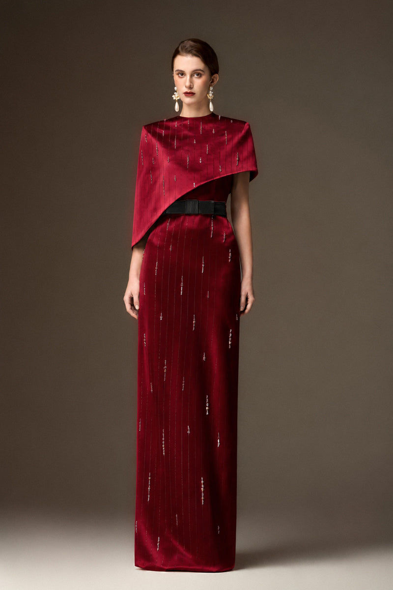 Red metallic asymmetric cape gown by I.H.F featuring a round neck and sleek column silhouette in dark red silk.