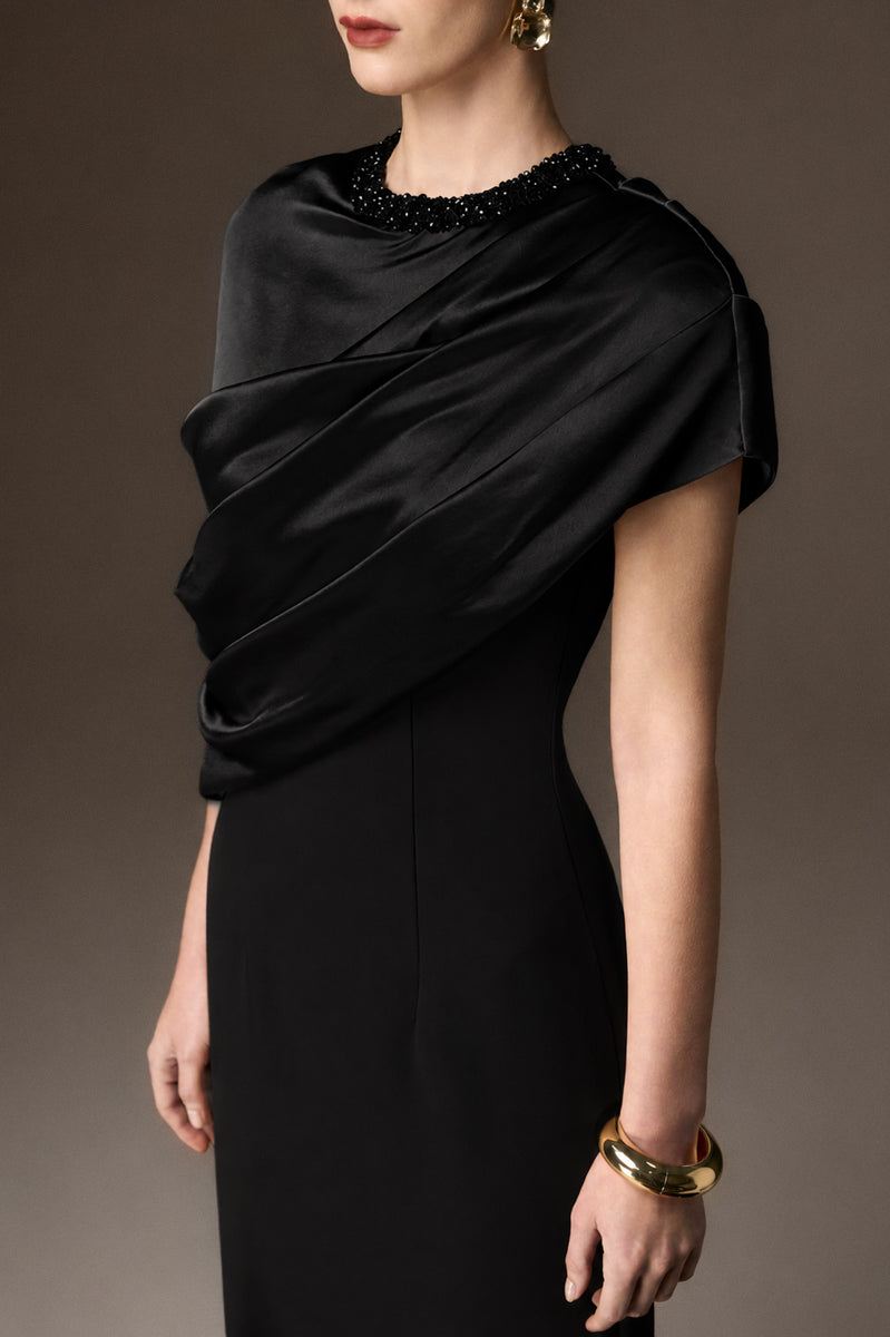 Black satin and crepe asymmetric cape gown by I.H.F featuring a round neckline and elegant column silhouette.
