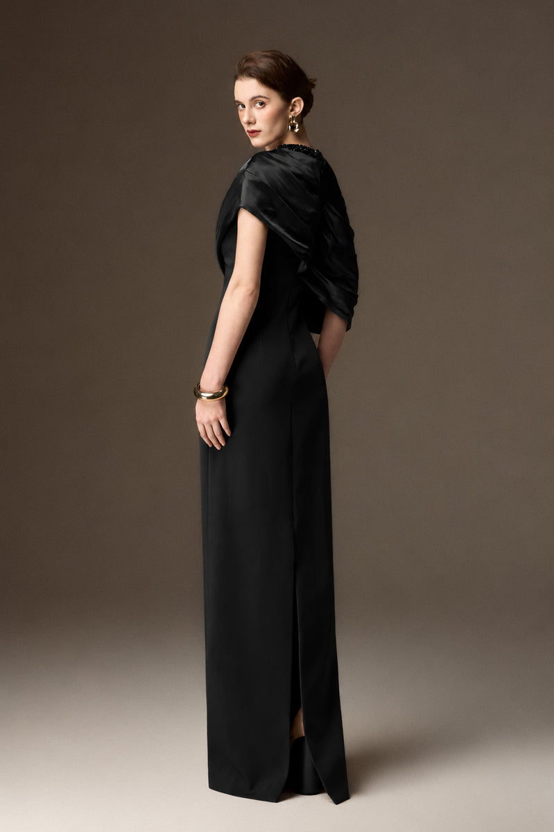 Black satin and crepe asymmetrical cape column gown by I.H.F, featuring a round neck and elegant drape.