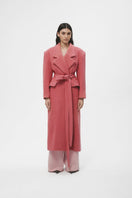 Pink wool maxi coat by JC Pajares hanging on a clothing rack, showcasing its long, cozy design and elegant texture.