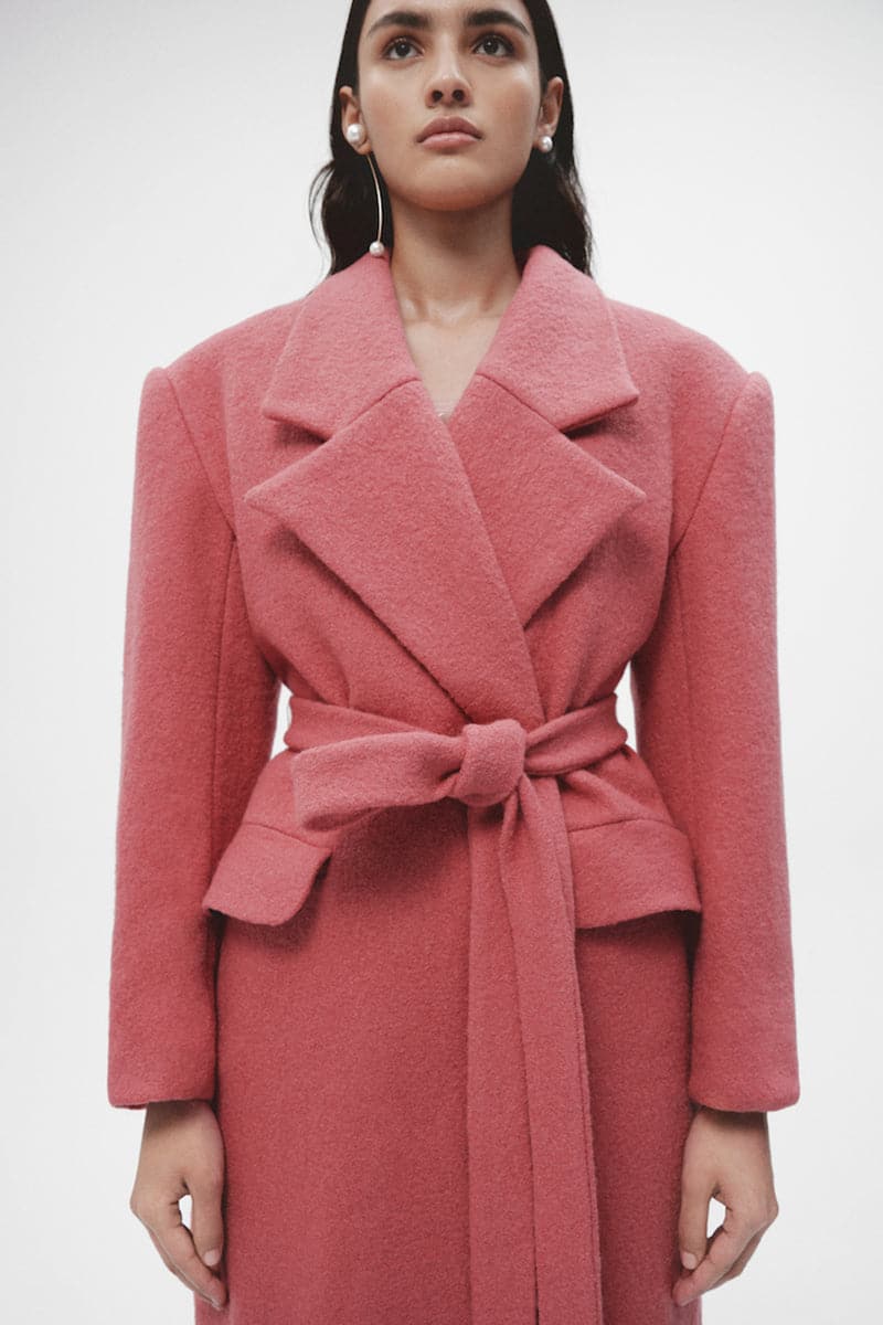 Pink wool maxi coat by JC Pajares, shown hanging on a rack with a tailored fit and long sleeves, perfect for winter wear.