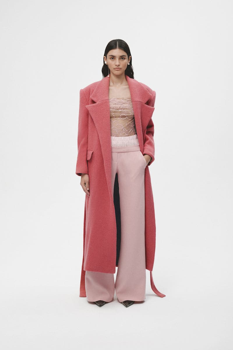 Pink wool maxi coat by JC Pajares displayed on a hanger, showcasing its long length and soft fabric texture.