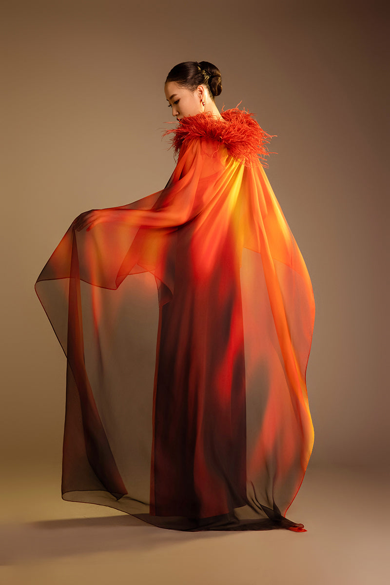 Orange printed gown with a detachable ostrich feather trim cape by Valenciani, showcasing elegant fabric and stylish design.