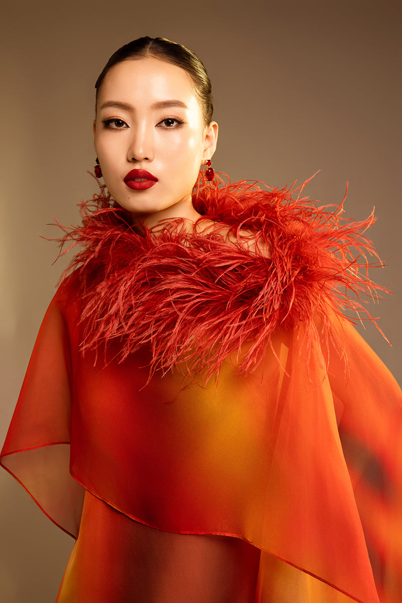 Orange printed gown with a detachable ostrich feather trim cape by Valenciani, showcasing elegant fabric and detailed design.