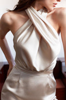 Elegant champagne-colored halter neck maxi dress by UNDRESS, featuring flowy fabric and sophisticated evening wear style.