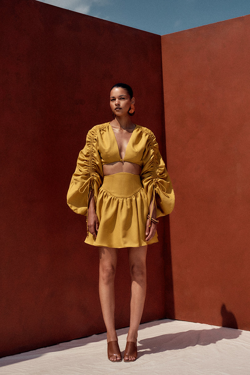 Bright gold Andrea Iyamah mini skirt with sleek fit, shown styled on a model in a fashion lookbook image.