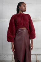 Maz Manuela Álvarez wine red accordion snail sweater hanging on a display, showcasing its textured knit and stylish design.