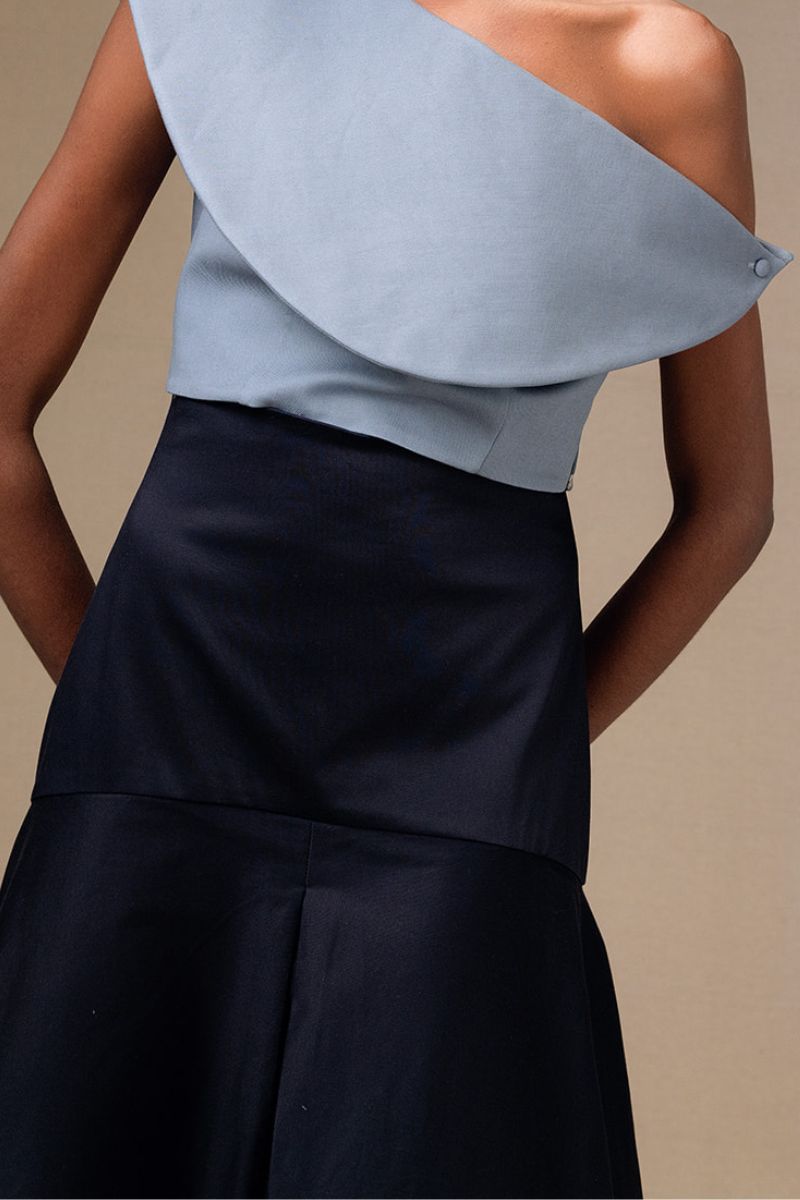 Navy blue ANA + MARIA midi skirt with a flowy silhouette and subtle pleats, shown on a model against a neutral background.