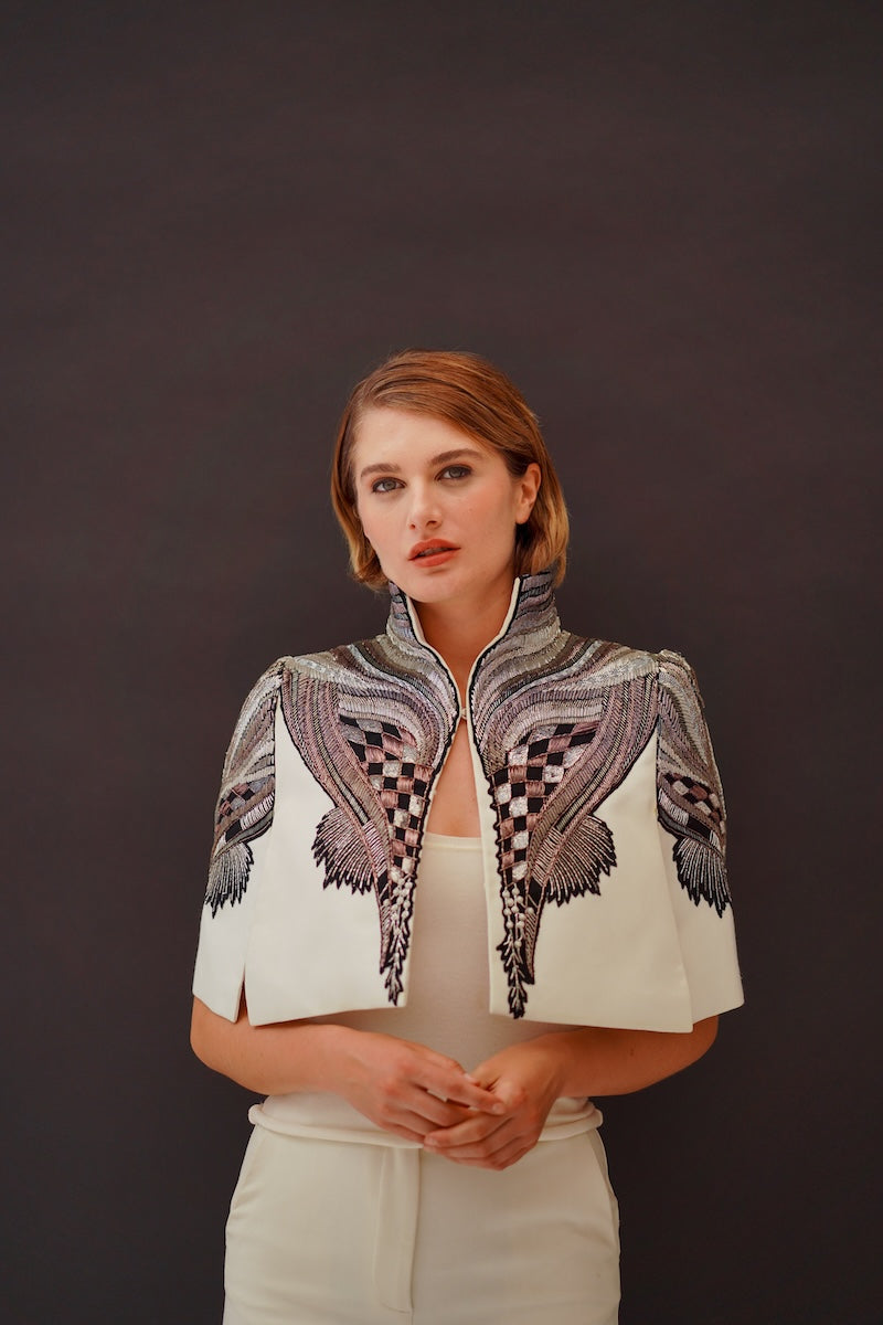 Ivory Nadya Shah All About Eve Capelet jacket with draped design and textured fabric, styled over a neutral outfit.