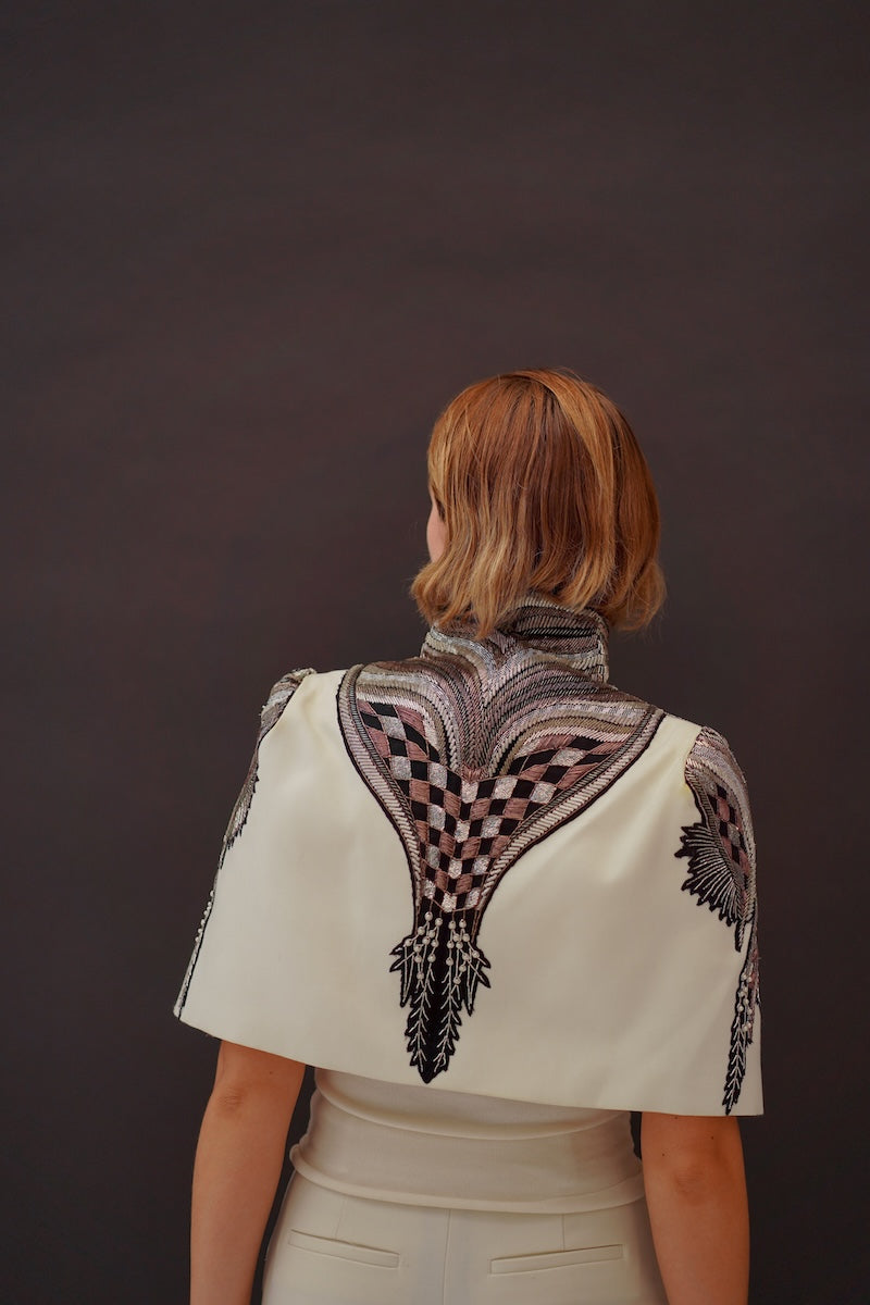 Ivory Nadya Shah All About Eve capelet jacket displayed on a hanger, showcasing its elegant, lightweight design and soft fabric.