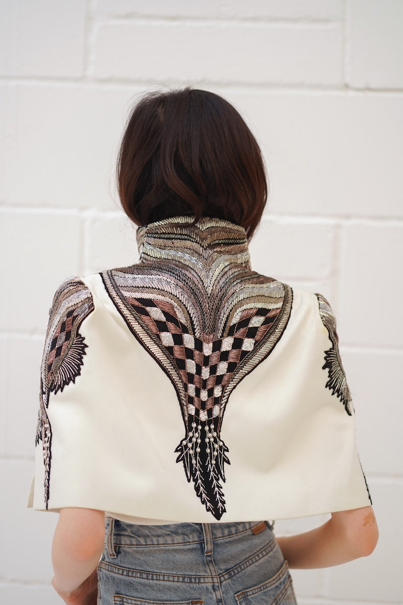 Ivory All About Eve capelet jacket by Nadya Shah, showcasing elegant fabric and detailed design on a neutral background.