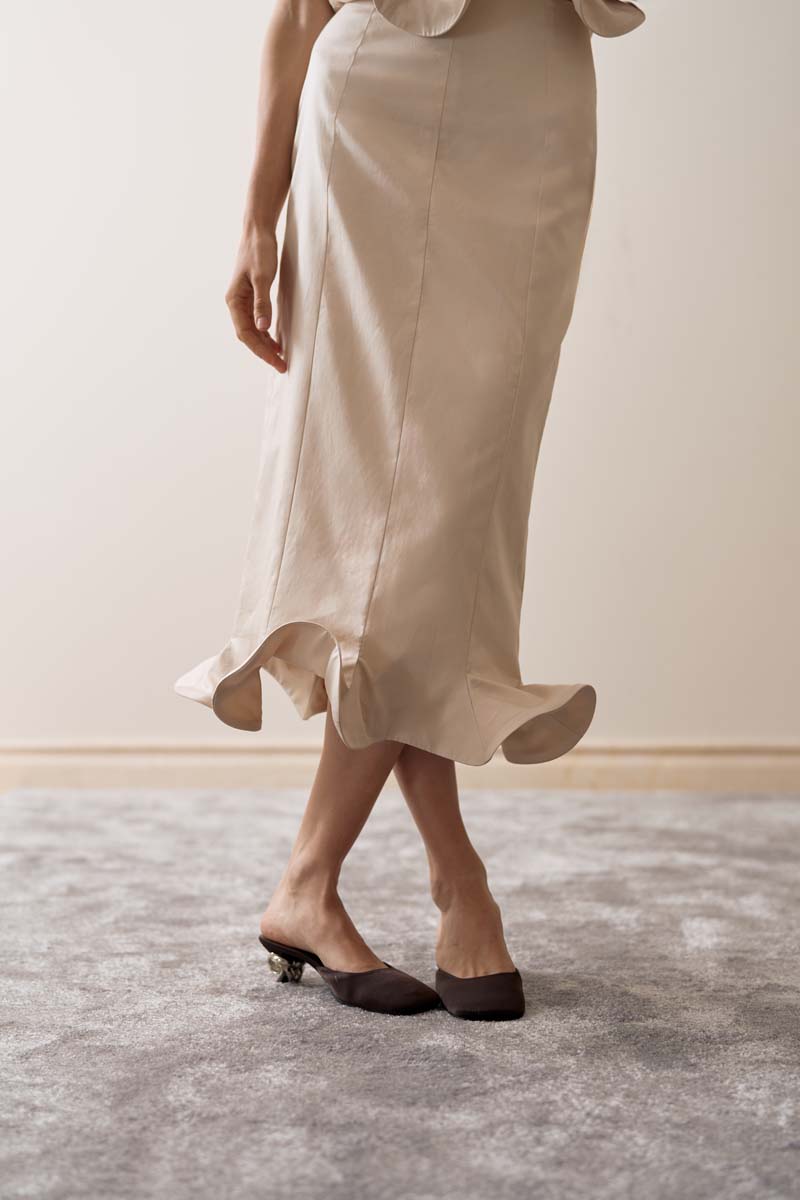Close-up of YASSMIN SALEH ivory arch midi skirt showcasing elegant fabric detail and sleek design.