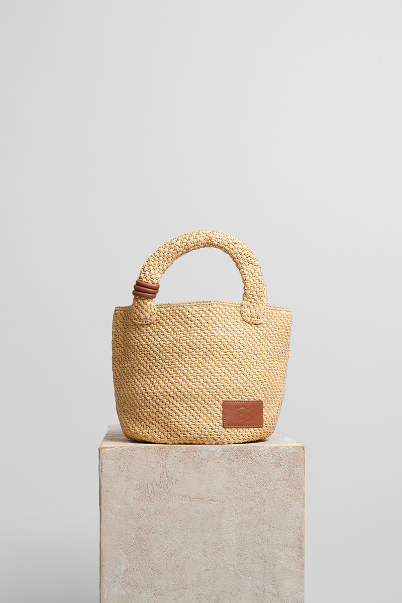 Beige raffia basket bag with top handle from Folklore The Label, showcasing natural woven texture and stylish design.
