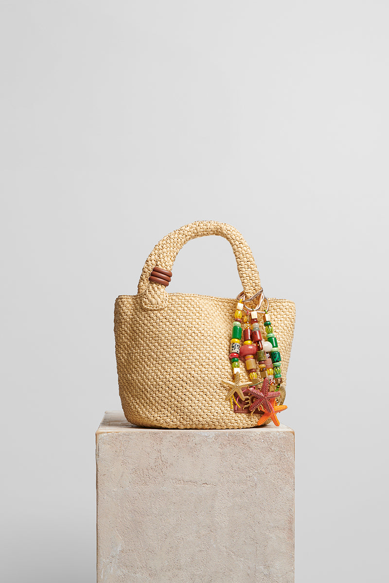 Beige raffia basket bag with top handle from Folklore The Label, showcasing its woven texture and stylish design.