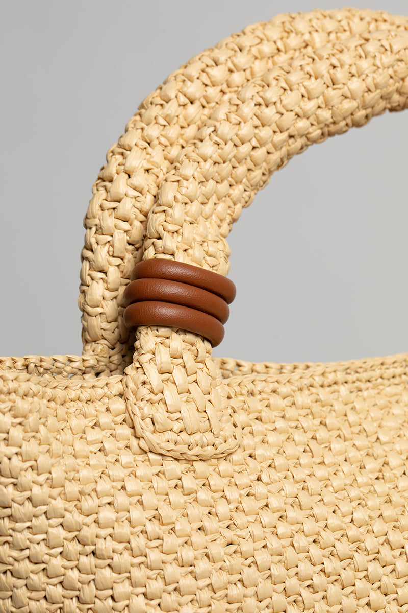 Beige raffia basket bag with top handle from Folklore The Label, showcasing its woven texture and stylish design.