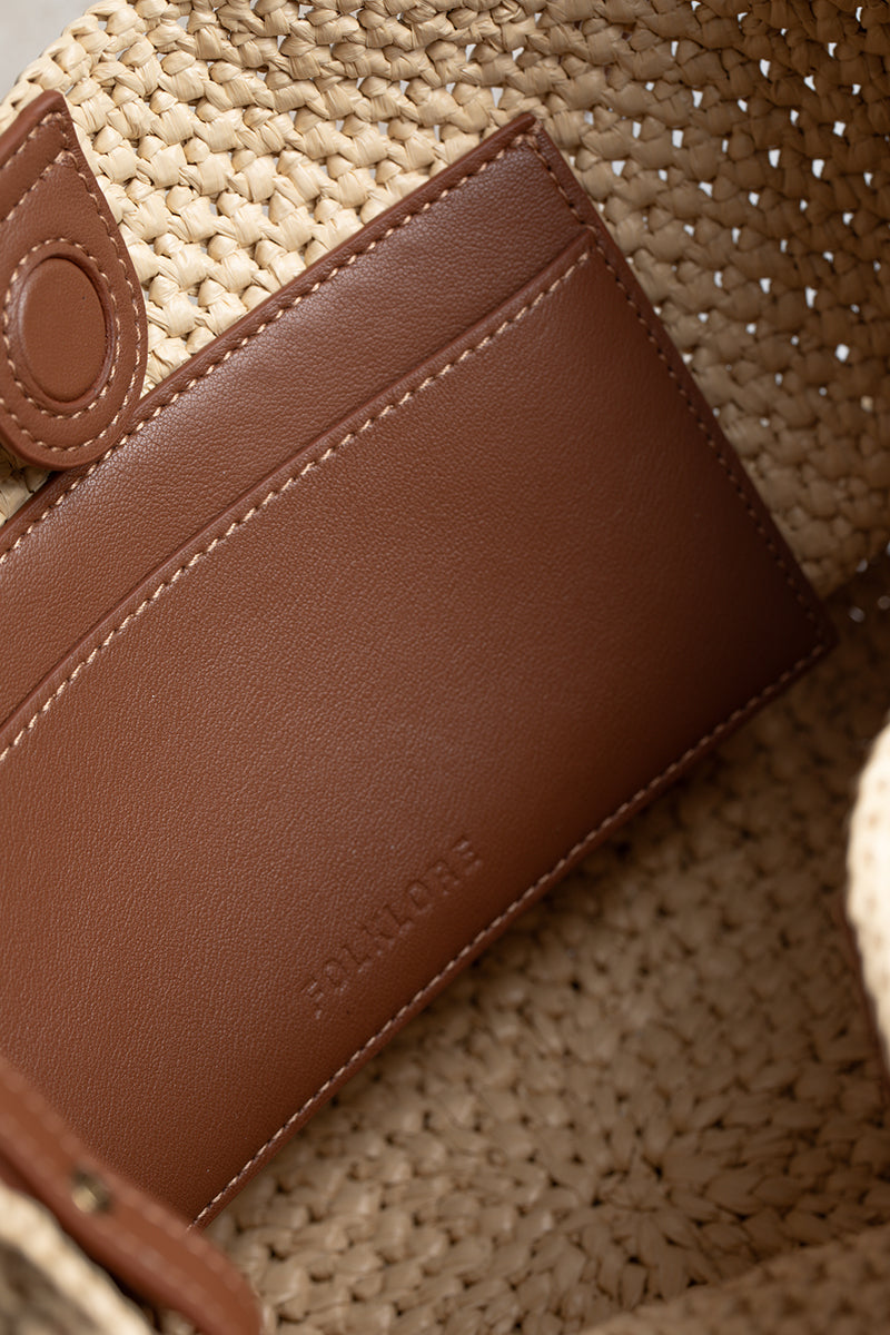 Beige raffia basket bag with top handle from Folklore The Label, showcasing a stylish and natural woven design.