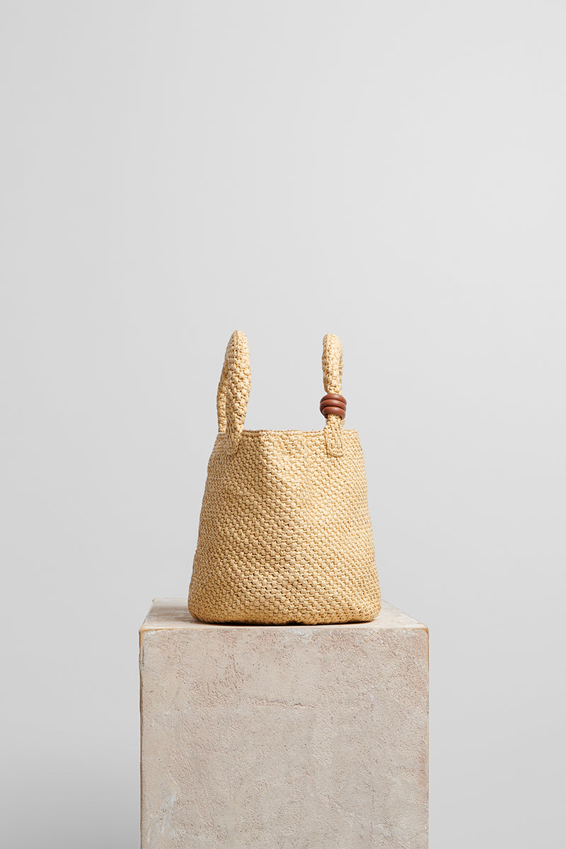 Beige raffia basket bag with top handle from Folklore The Label, showcasing natural woven texture and stylish design.