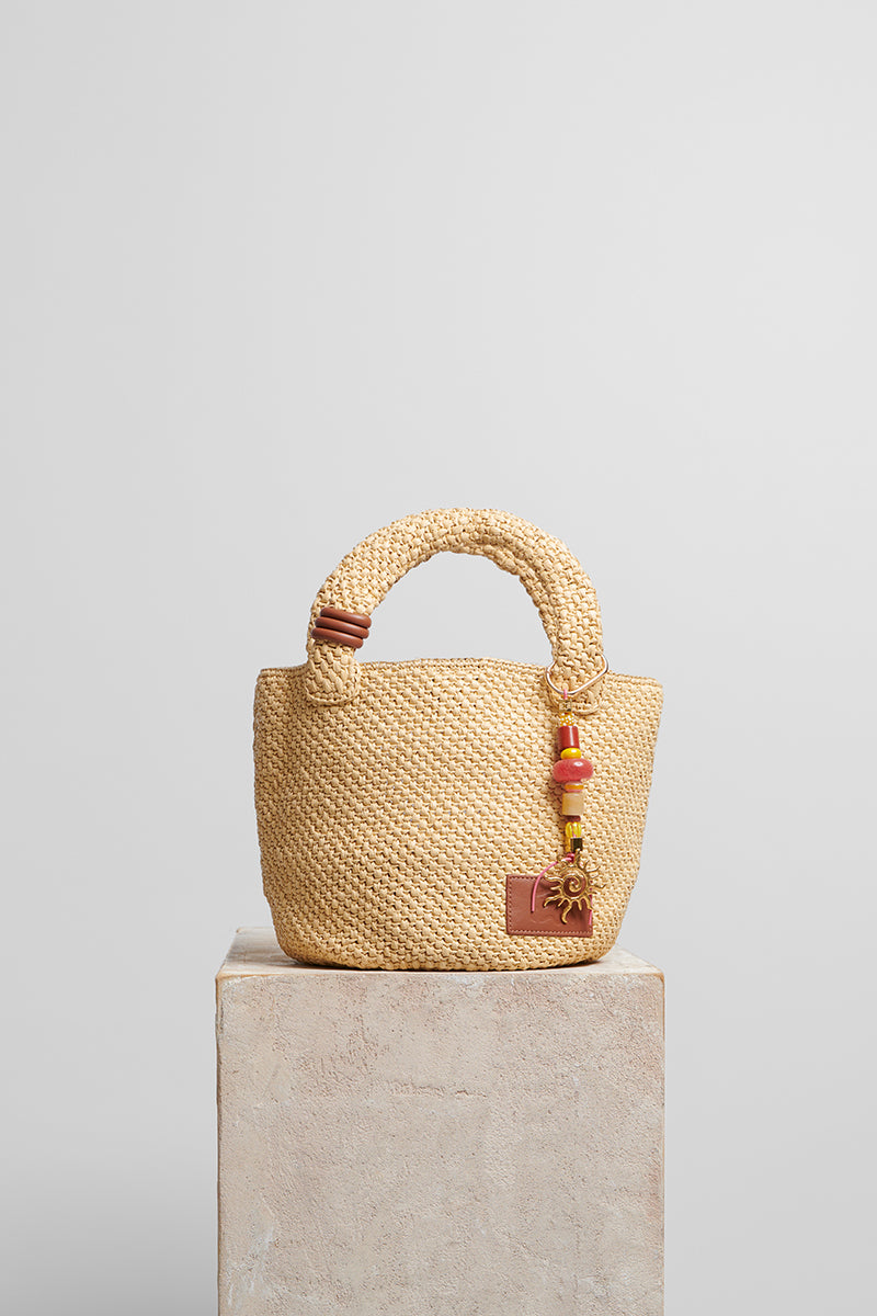 Beige raffia basket bag with top handles by Folklore The Label, featuring a woven texture and casual, stylish design.