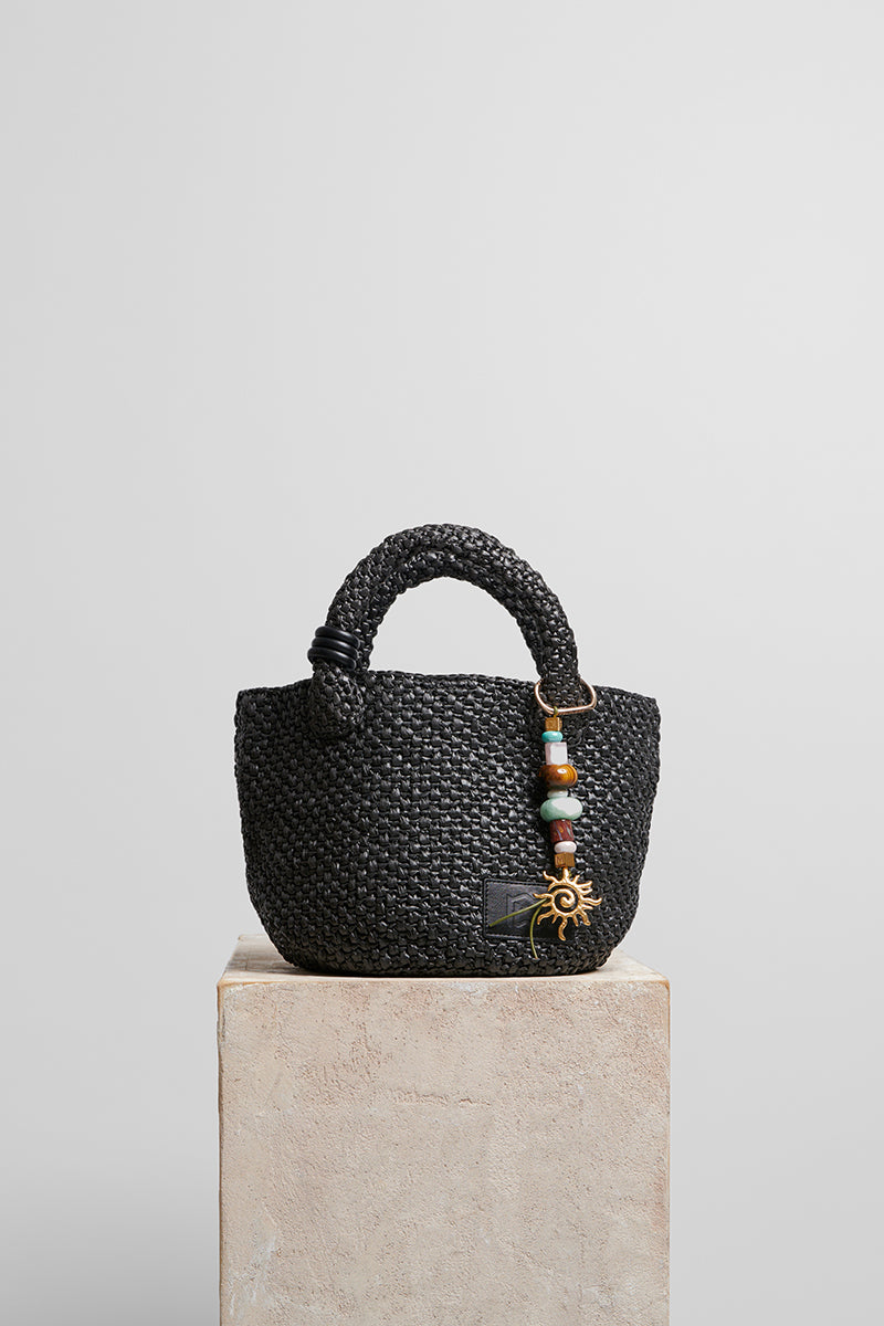Black raffia basket bag with top handle from Folklore The Label, featuring a woven, textured design ideal for casual or chic occasions.