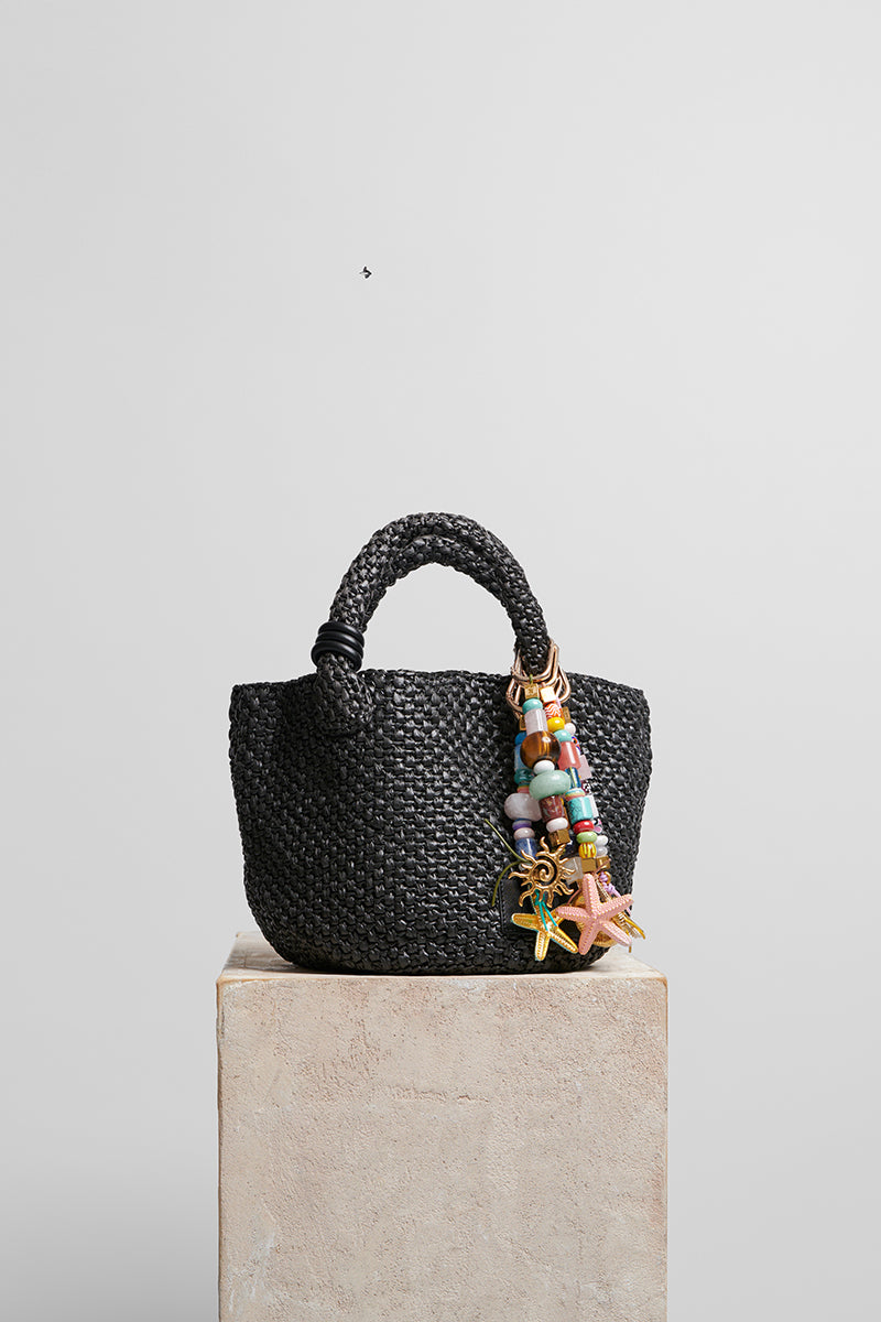 Black raffia basket bag with top handle from FolkLore The Label, showcasing a stylish woven design.