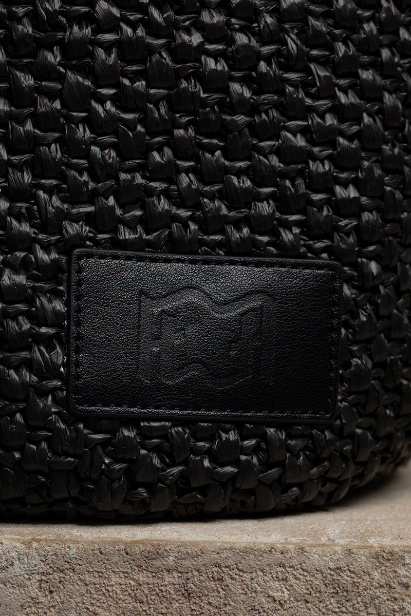Black raffia basket bag with top handle from Folklore The Label, showcasing woven texture and stylish design.