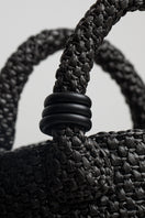 Black raffia basket-style top handle bag from Folklore The Label, featuring a woven design and sturdy handle.