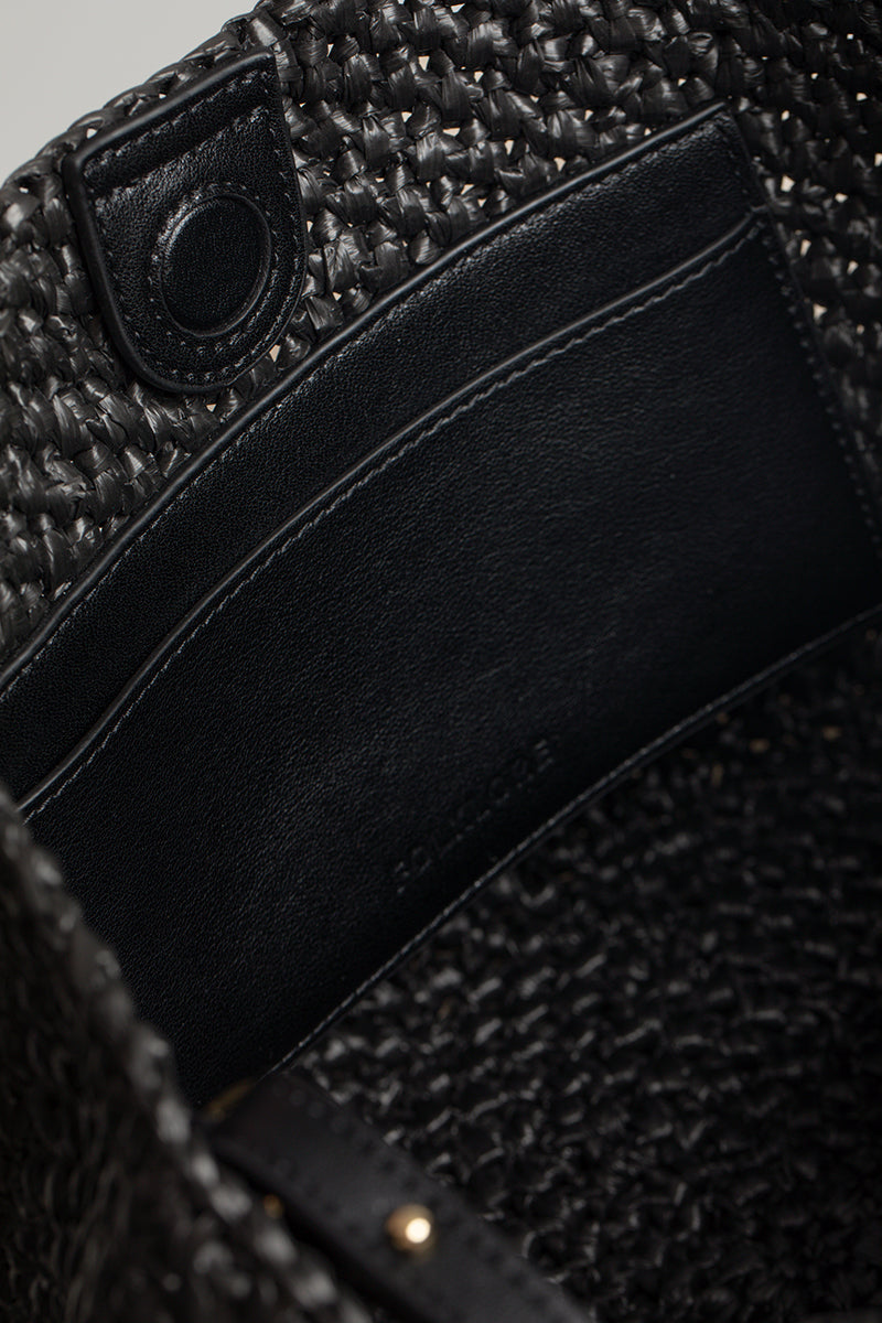 Black raffia basket bag with top handle from FolkLore The Label, featuring a woven design and stylish, natural texture.
