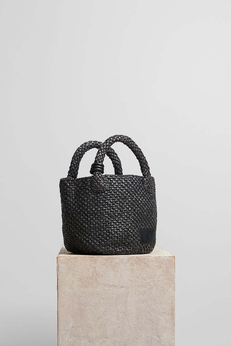 Black raffia basket bag with top handle from FolkLore The Label, featuring a woven design and spacious interior.