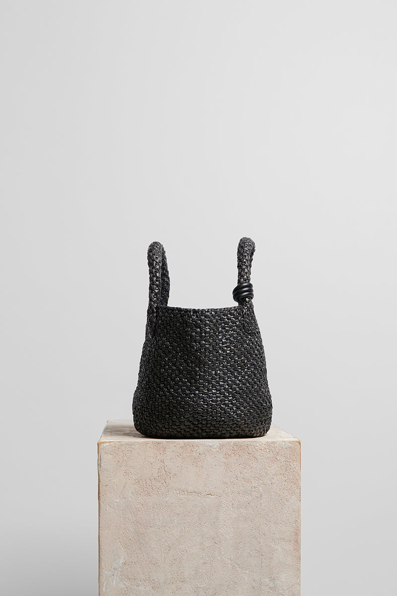 Black raffia basket bag with top handle from FolkLore The Label, featuring a woven design and spacious interior.
