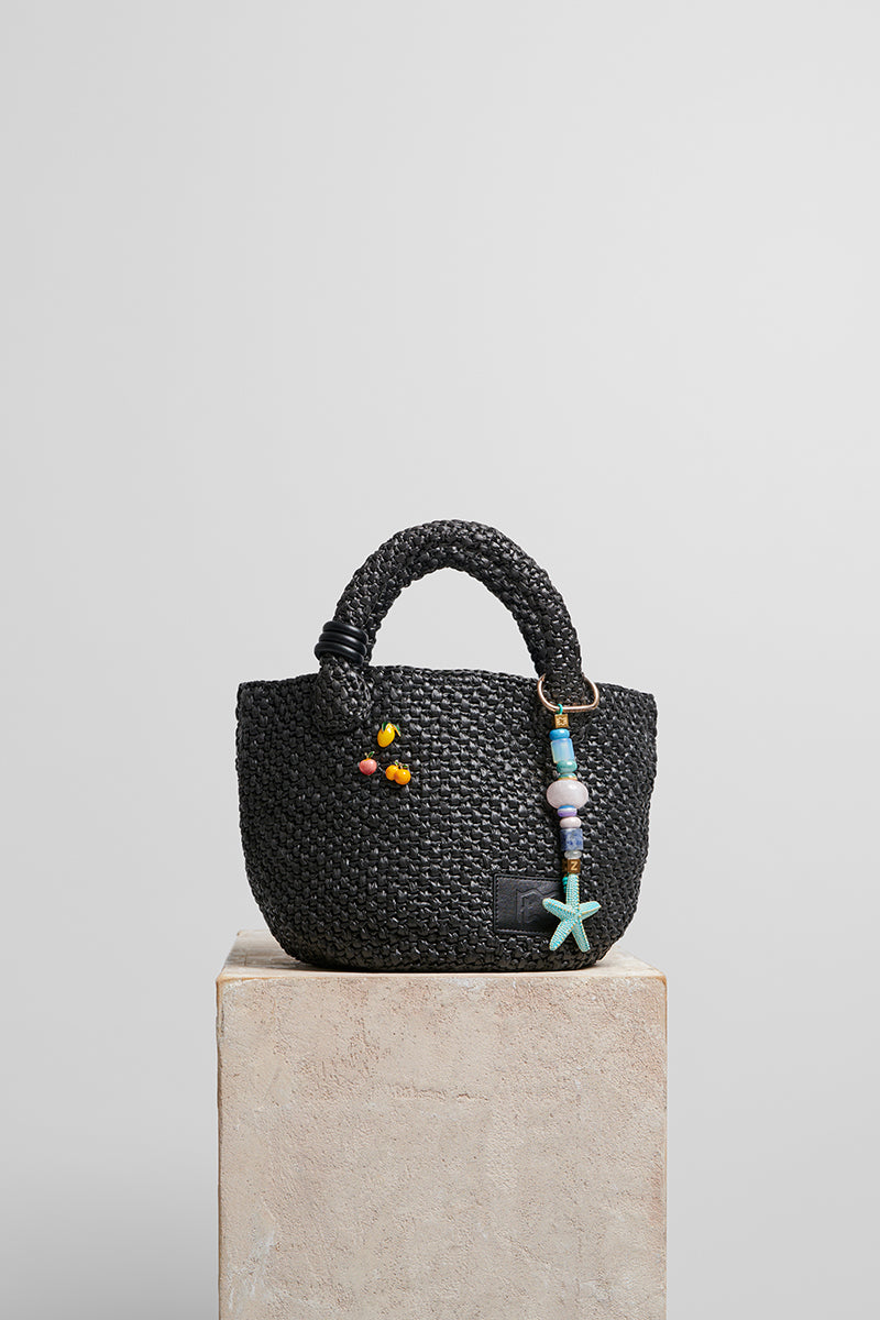 Black raffia basket bag with top handle from Folklore The Label, featuring a woven design and stylish, natural look.