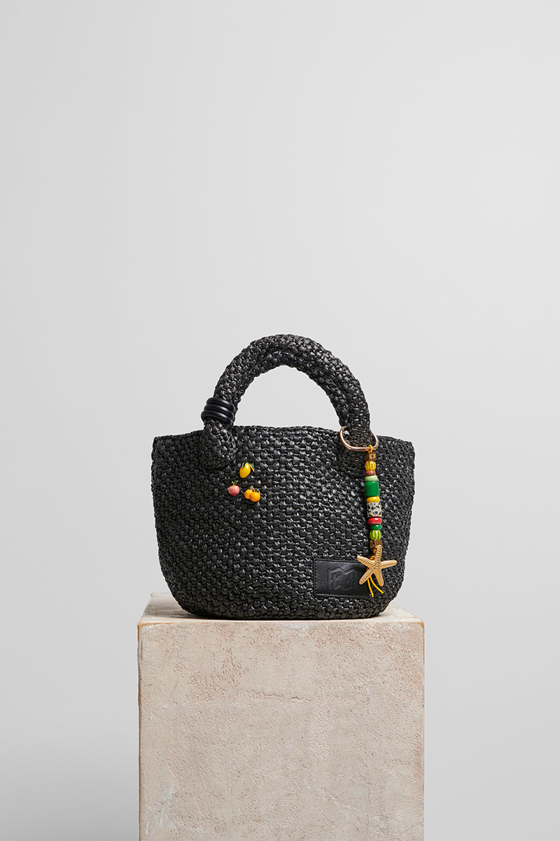 Black raffia basket bag with top handle from FolkLore The Label, featuring woven texture and stylish design.