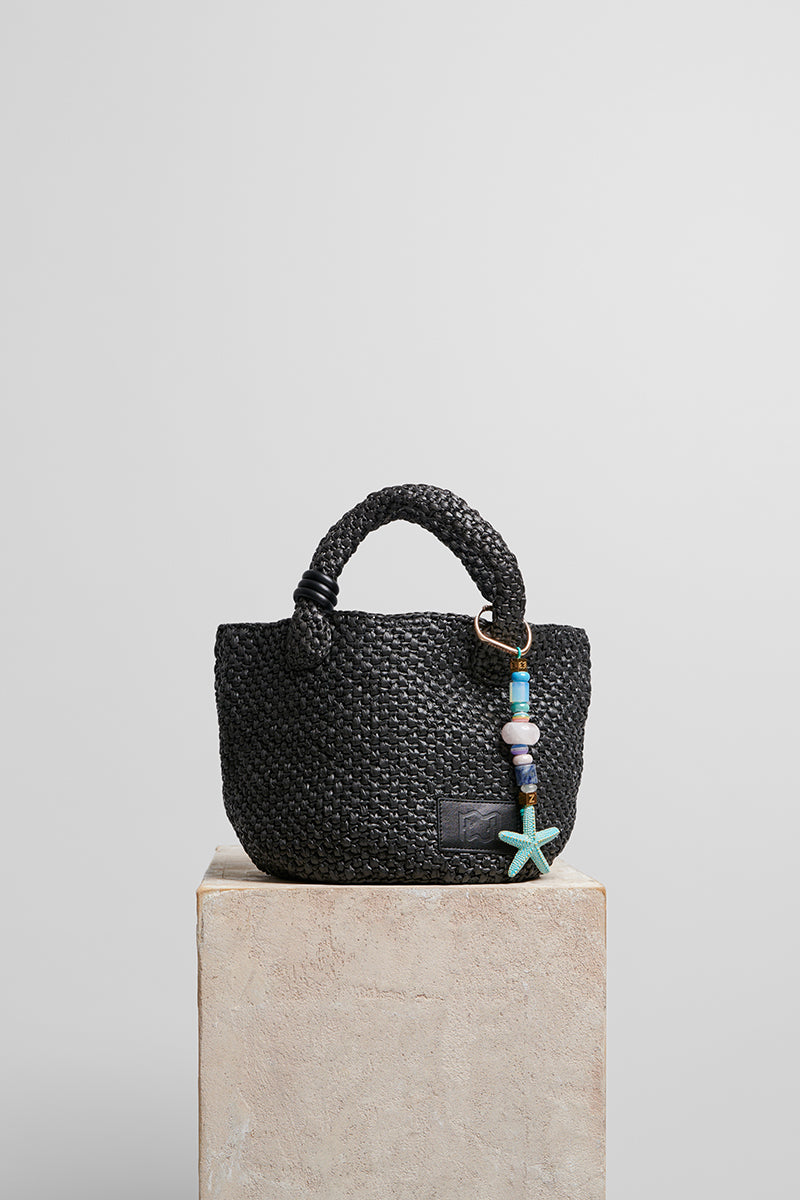 Black raffia basket bag with top handle from Folklore The Label, showcasing woven texture and stylish design.