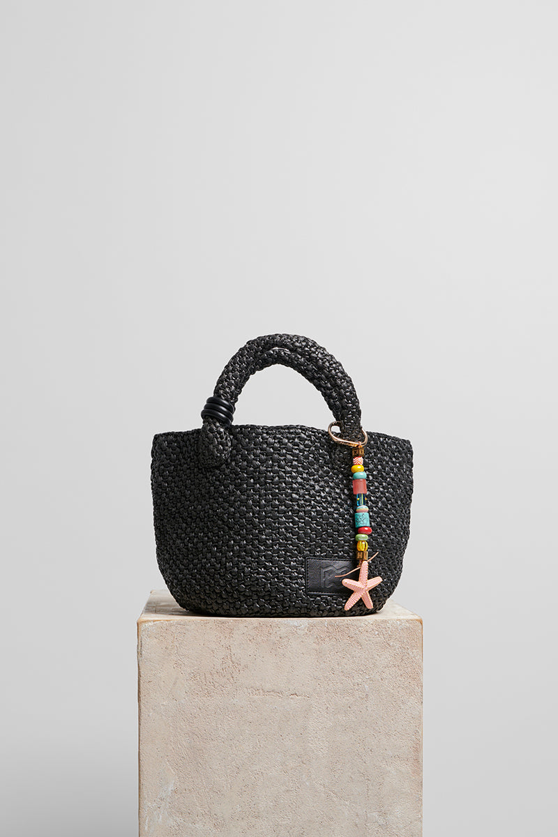 Black raffia basket bag with top handle from Folklore The Label, featuring a woven design and spacious interior.
