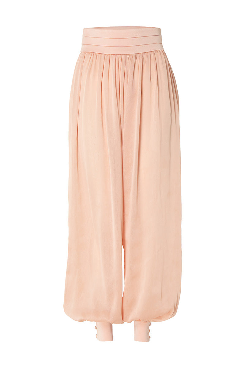 Studio NK Bloom peach pants with a relaxed fit and wide-leg style, shown on a model in a casual outdoor setting.