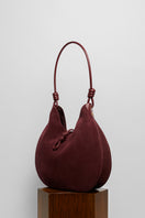 Maroon suede boho shoulder bag by Folklore The Label with tassel accents and adjustable strap.