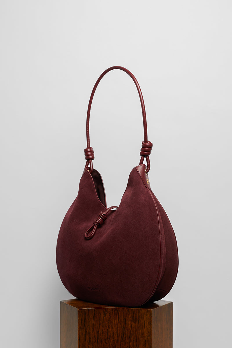 Maroon suede boho shoulder bag by Folklore The Label with tassel accents and adjustable strap.